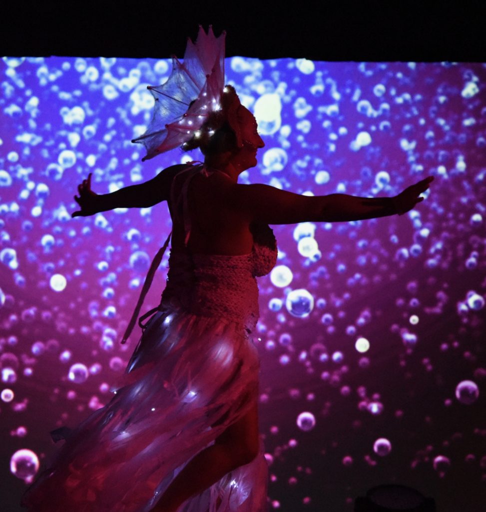 Costume of light with a background of light spots in the 2018 Big Sur Fashion Show, a cultural encounter with the spirit of community. (Image © Meredith Mullins.)