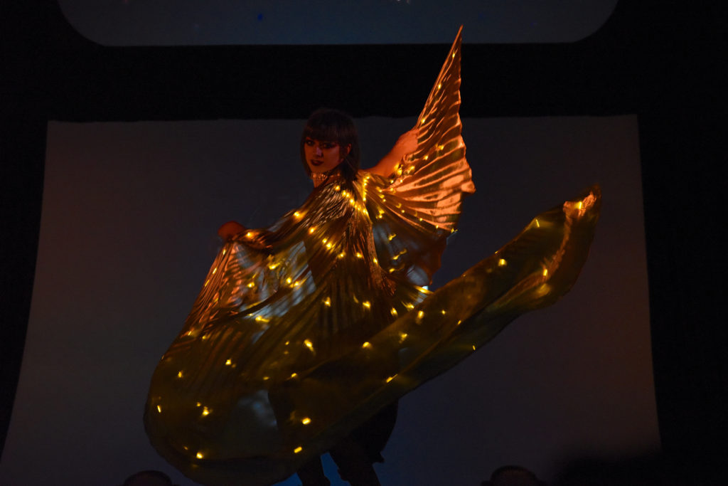 Dancer with gold wings performing at the 2018 Bug Sur Fashion Show, a cultural encounter with the spirit of community. (Image © Meredith Mullins.)